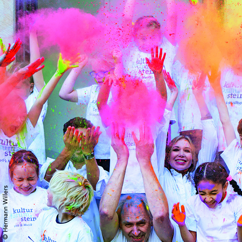 Lehrkräfte und Schüler/innen des KulturForumSteinfurt werfen Holi-Pulver in die Luft